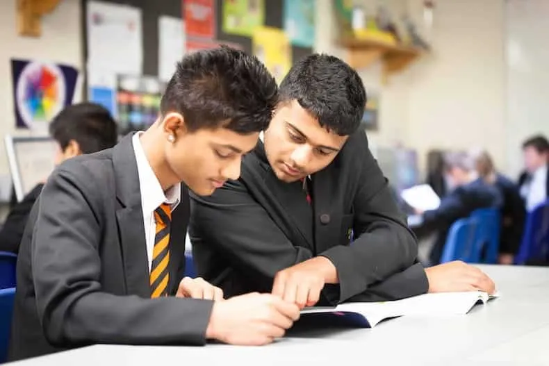 Two secondary school students working together on a textbook in a classroom.